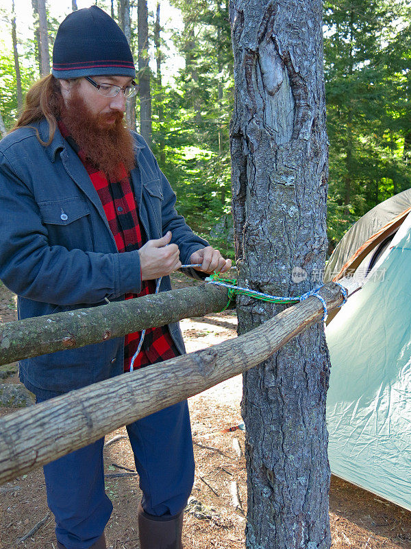 Lumbersexual Hipster Camping Man Tying Rope for Makeshift Tree Table